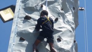 Image shows a child climbing a rock wall while wearing a harness and clipped in to safety ropes.